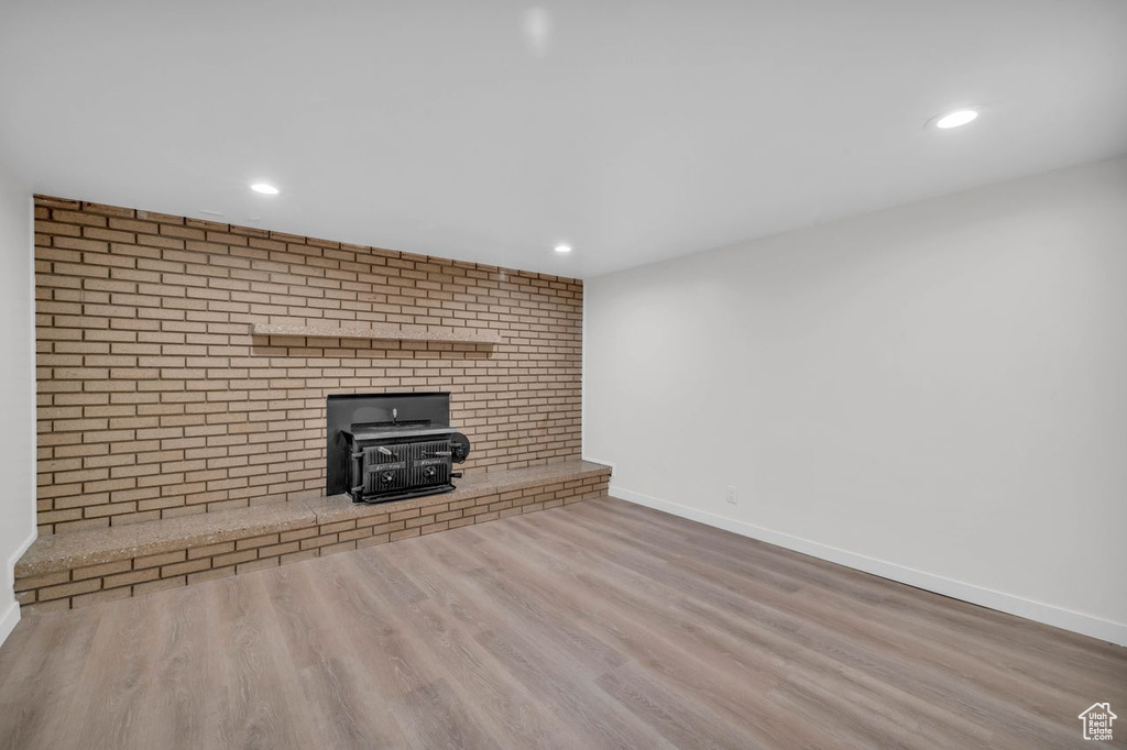Unfurnished living room featuring wood-type flooring, brick wall, a wood stove, and a fireplace