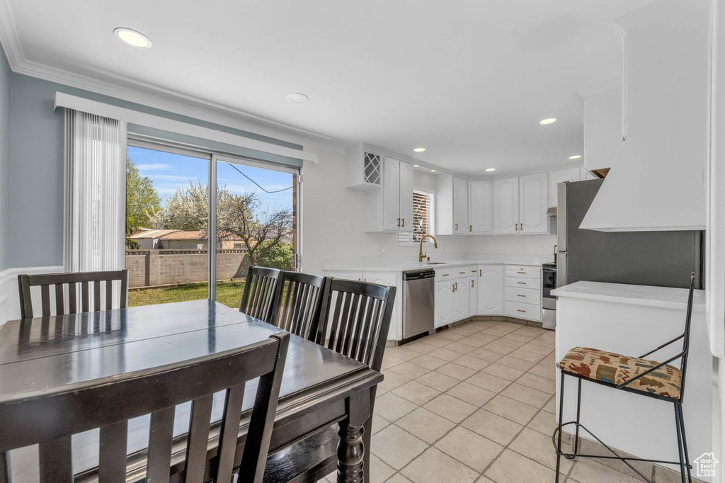 Kitchen with appliances with stainless steel finishes, white cabinets, sink, light tile floors, and ornamental molding