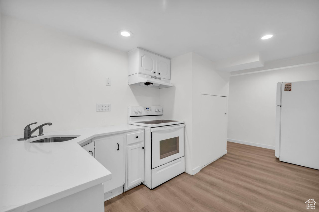 Kitchen with sink, white appliances, light wood-type flooring, and white cabinetry