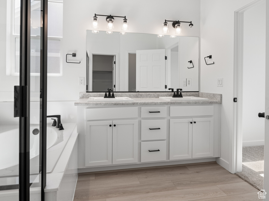 Bathroom featuring hardwood / wood-style flooring, dual bowl vanity, and a bathing tub