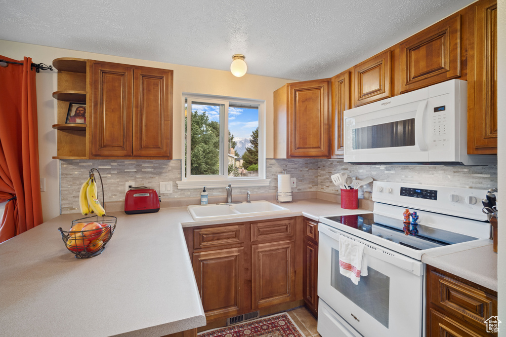 Kitchen featuring a textured ceiling, white appliances, tasteful backsplash, and sink