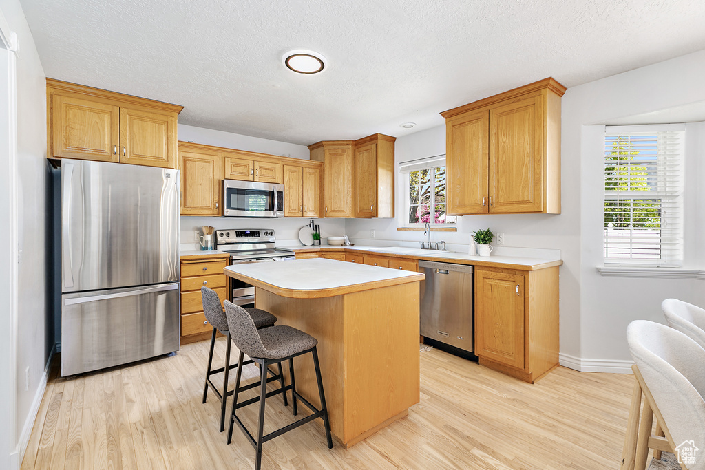 Kitchen featuring stainless steel appliances, sink, a breakfast bar area, a kitchen island, and light hardwood / wood-style floors
