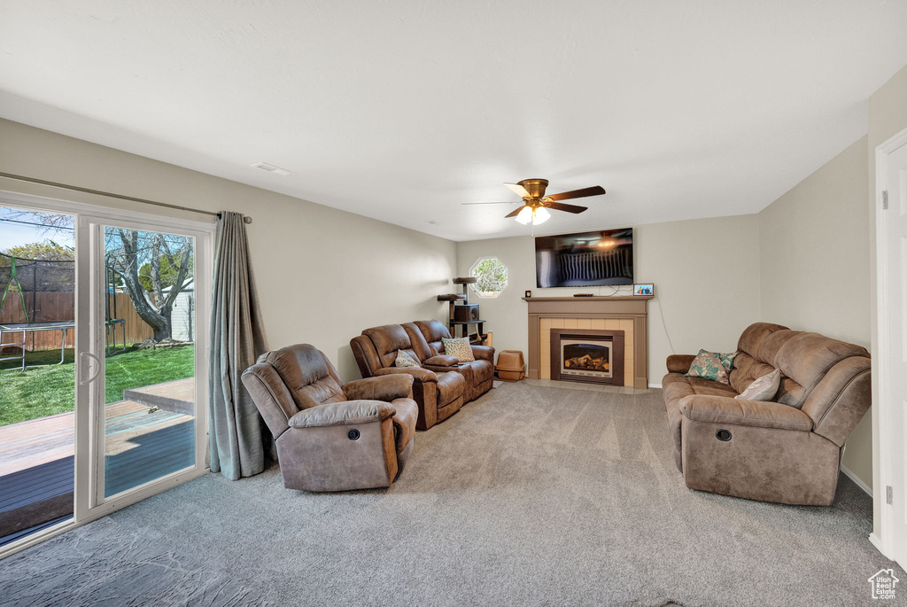 Carpeted living room featuring a tiled fireplace and ceiling fan