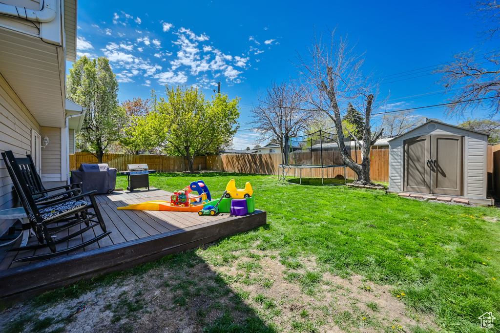 View of yard featuring a deck, a trampoline, and a storage unit