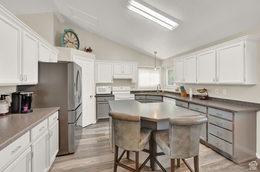 Kitchen featuring vaulted ceiling, white appliances, light hardwood / wood-style floors, and a center island