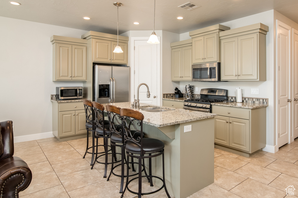Kitchen featuring stainless steel appliances, a kitchen island with sink, sink, pendant lighting, and light tile floors