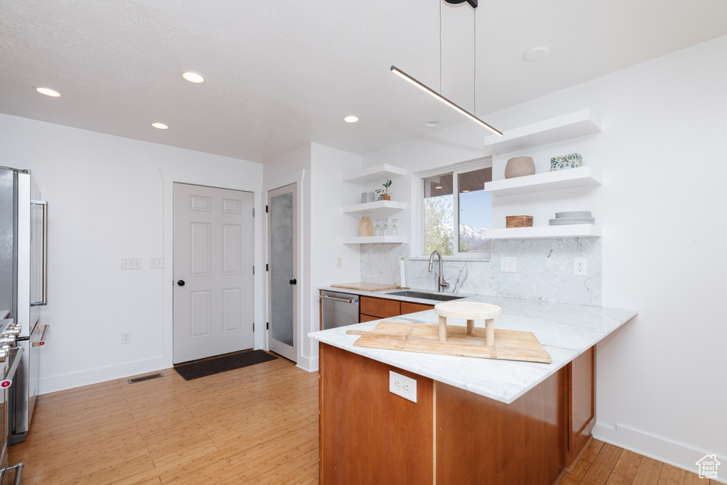 Kitchen featuring sink, backsplash, stainless steel dishwasher, light hardwood / wood-style flooring, and kitchen peninsula