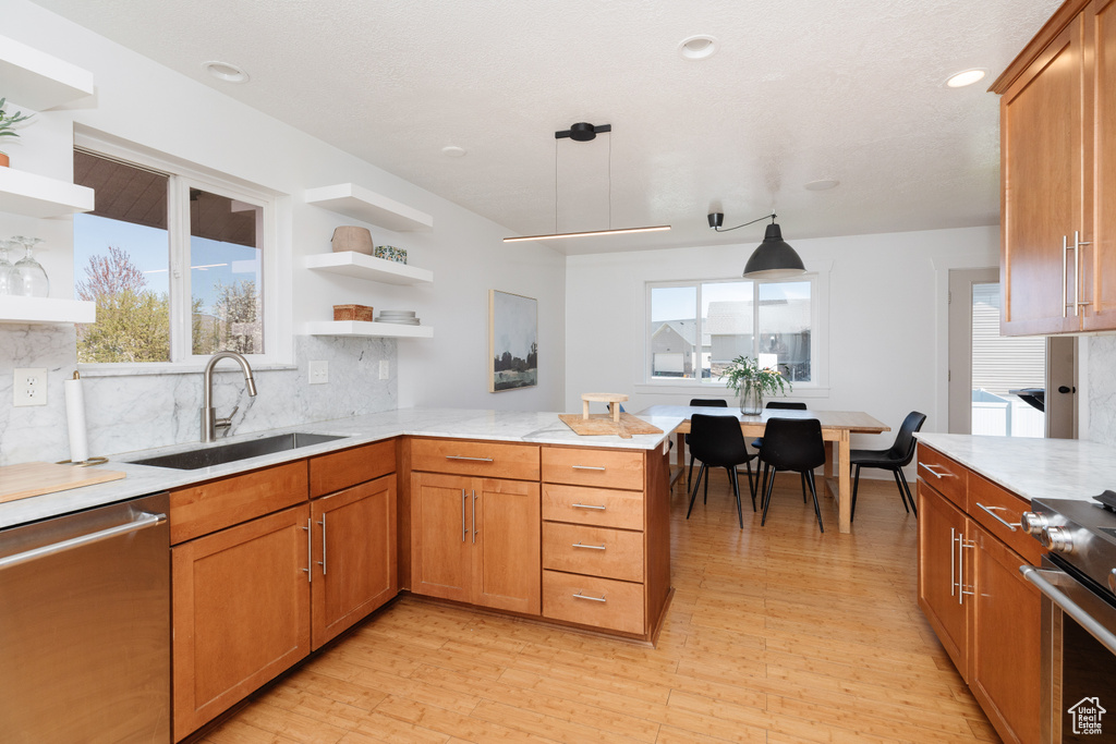 Kitchen with decorative light fixtures, backsplash, stainless steel appliances, light hardwood / wood-style floors, and sink
