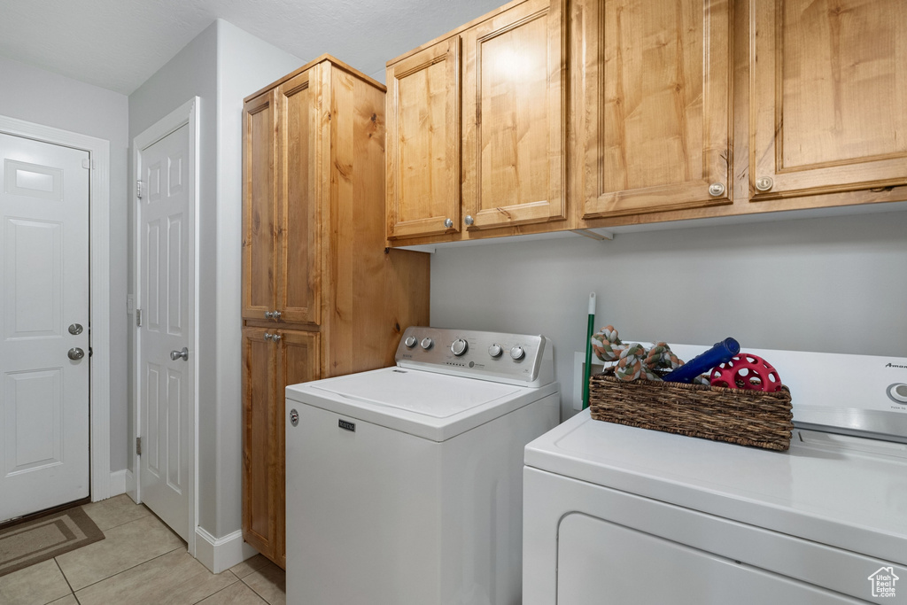 Clothes washing area featuring independent washer and dryer, cabinets, and light tile floors
