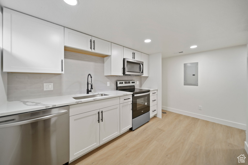 Kitchen with appliances with stainless steel finishes, light hardwood / wood-style floors, tasteful backsplash, white cabinets, and sink