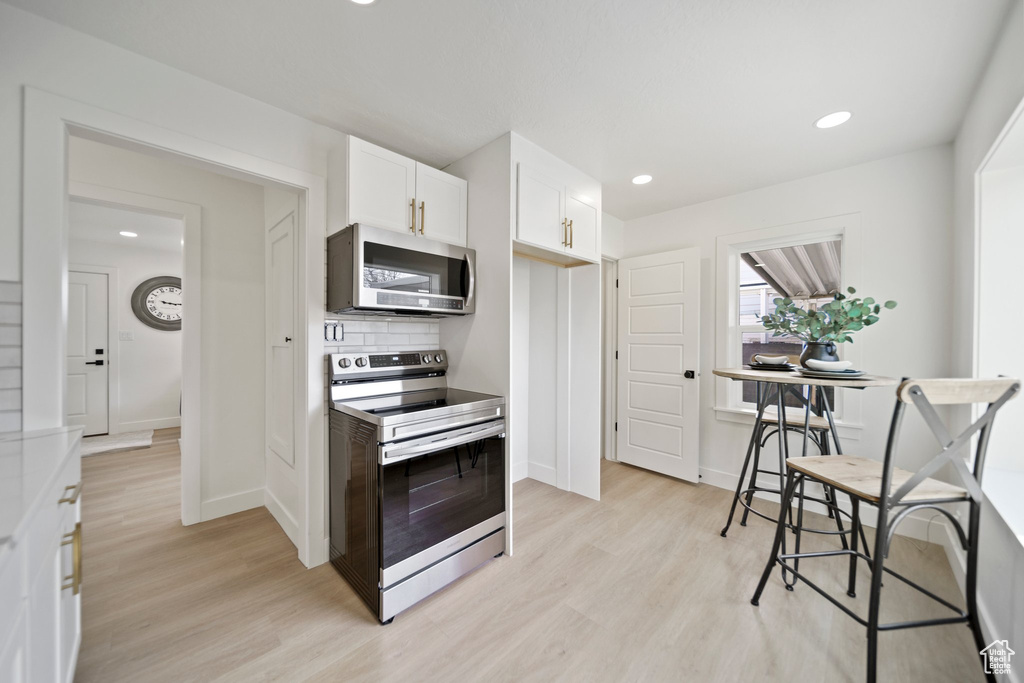 Kitchen featuring light hardwood / wood-style floors, backsplash, white cabinetry, and electric range