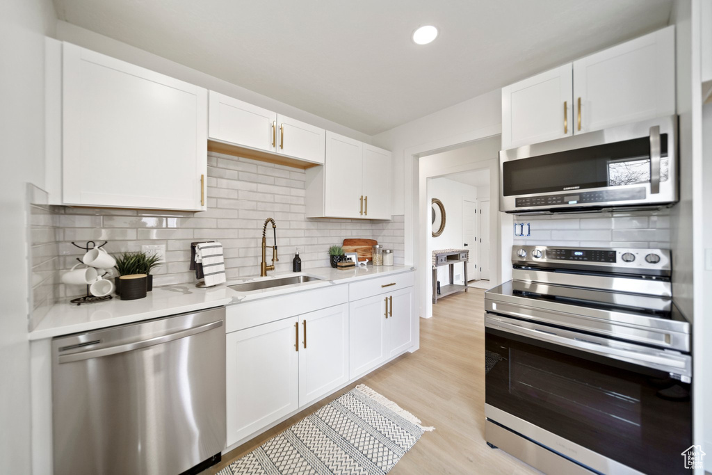 Kitchen with sink, backsplash, white cabinetry, stainless steel appliances, and light hardwood / wood-style flooring