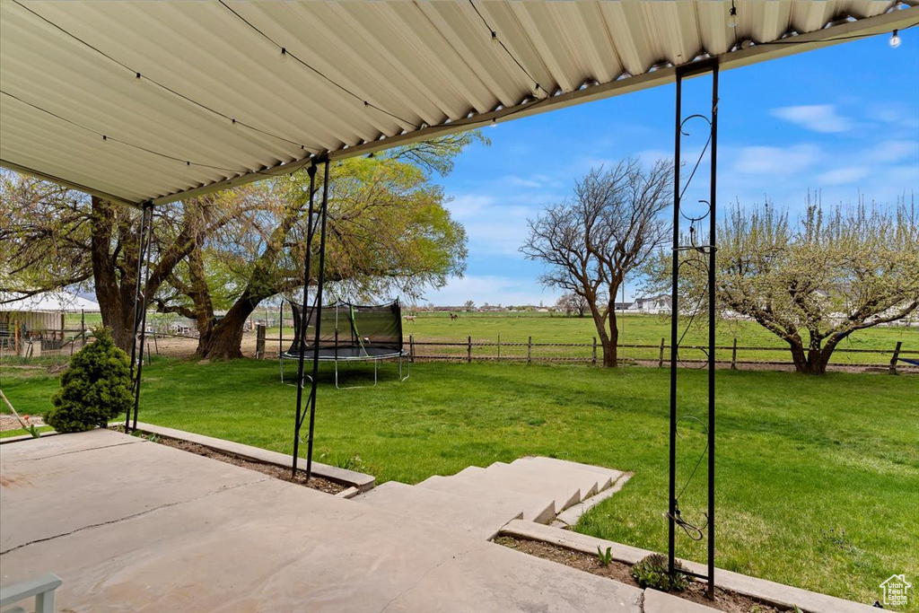 Exterior space featuring a patio area, a rural view, a trampoline, and a lawn