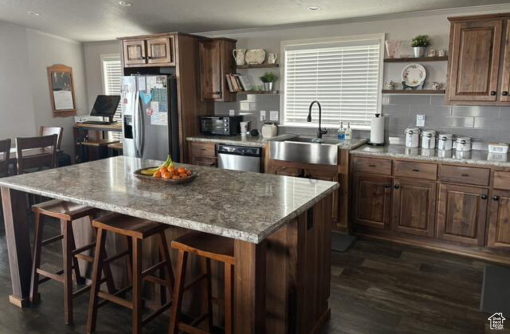 Kitchen with a center island, sink, tasteful backsplash, dark wood-type flooring, and stainless steel appliances