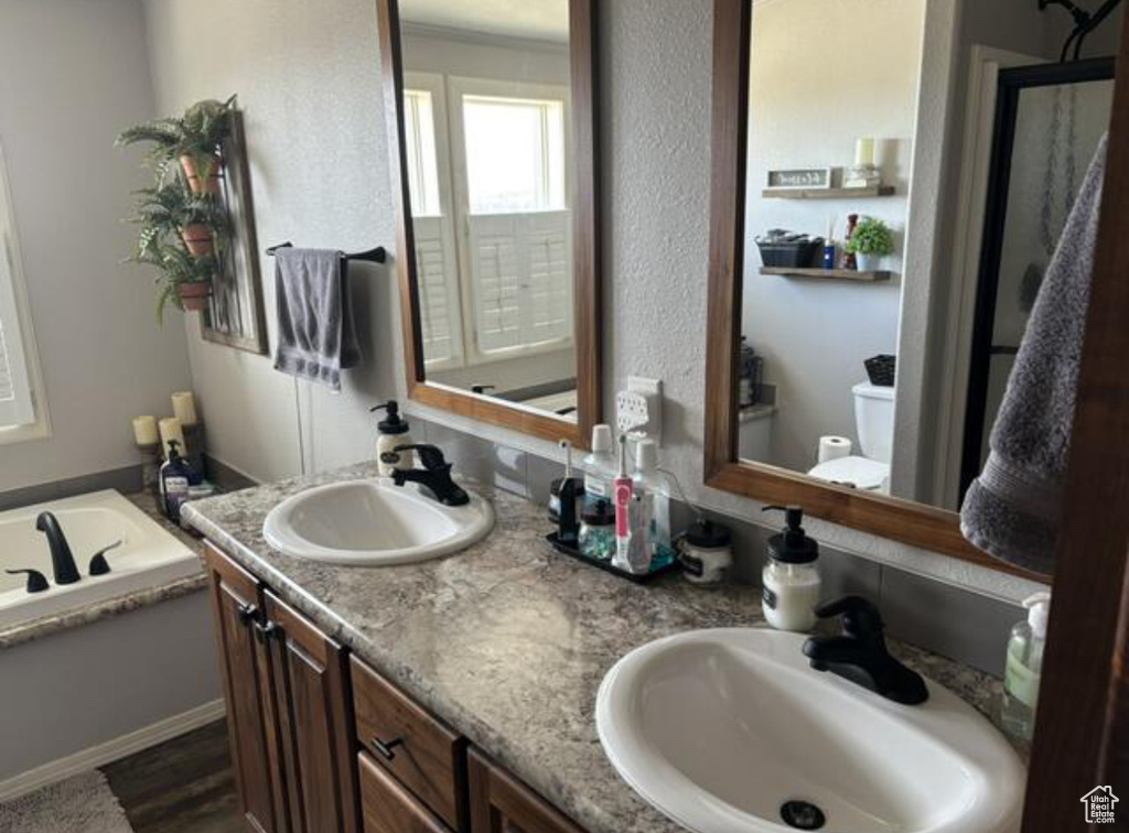 Bathroom featuring hardwood / wood-style flooring, toilet, dual vanity, and a bath