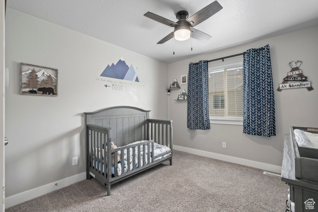 Bedroom featuring carpet flooring, ceiling fan, and a crib