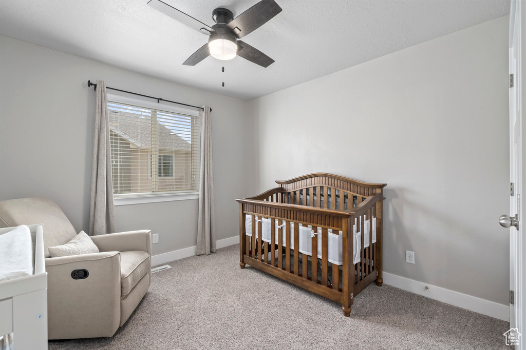 Bedroom featuring ceiling fan, light carpet, and a crib