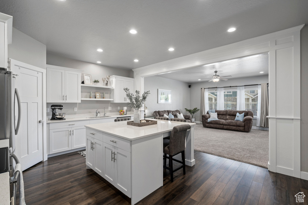 Kitchen featuring dark colored carpet, ceiling fan, white cabinets, and a kitchen bar
