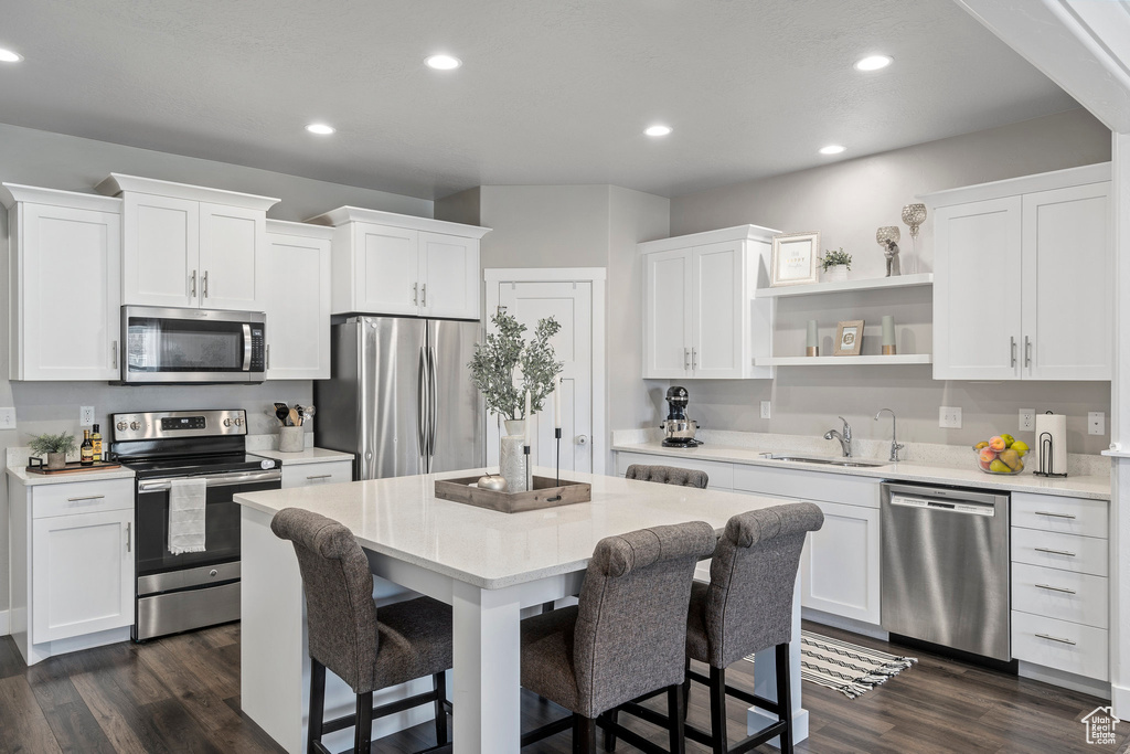 Kitchen with white cabinets, appliances with stainless steel finishes, a kitchen island, and dark wood-type flooring