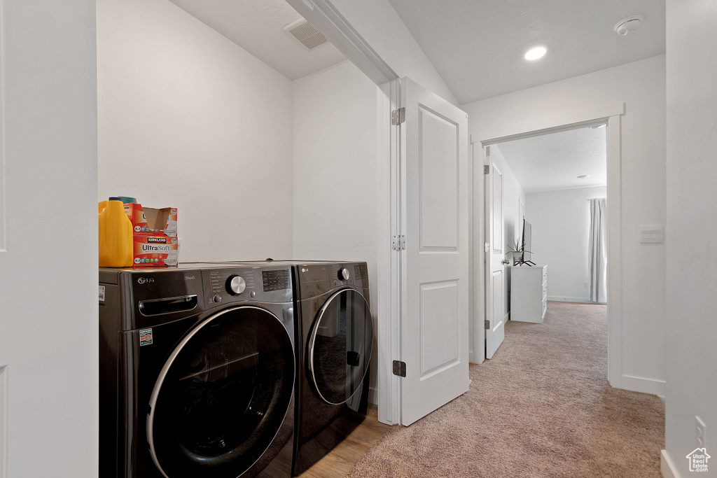 Clothes washing area with light colored carpet and washer and clothes dryer