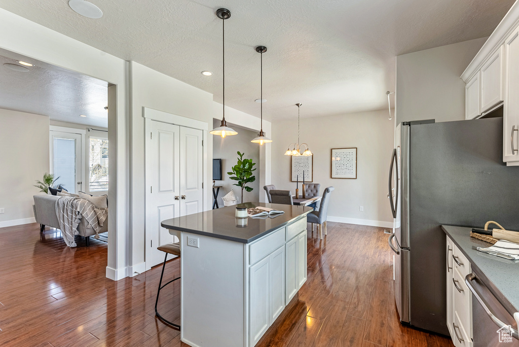 Kitchen with appliances with stainless steel finishes, white cabinets, dark wood-type flooring, hanging light fixtures, and a kitchen breakfast bar