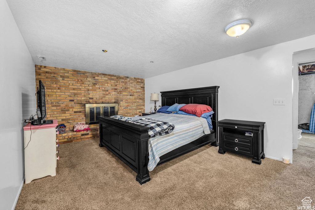 Carpeted bedroom featuring brick wall, a fireplace, and a textured ceiling