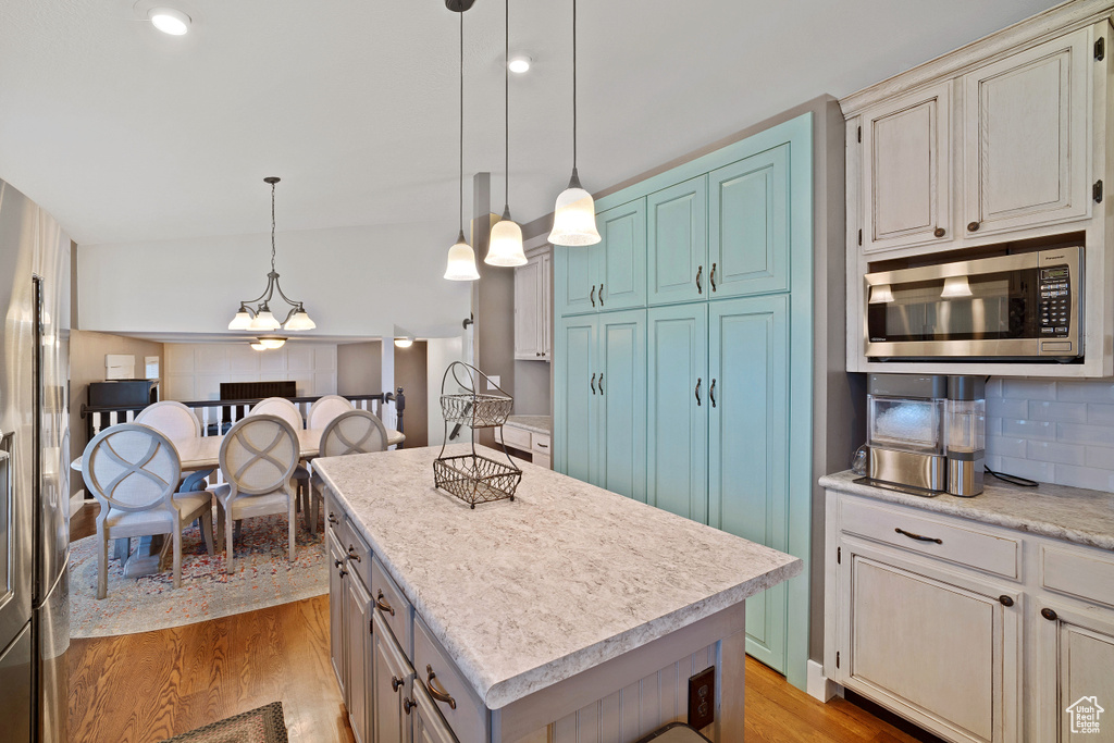 Kitchen featuring light wood-type flooring, decorative light fixtures, a kitchen island, stainless steel appliances, and an inviting chandelier