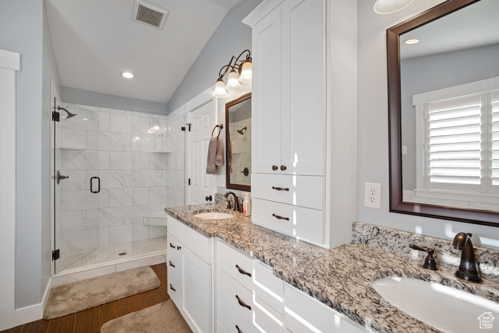 Bathroom with a shower with door, hardwood / wood-style floors, vaulted ceiling, and double sink vanity