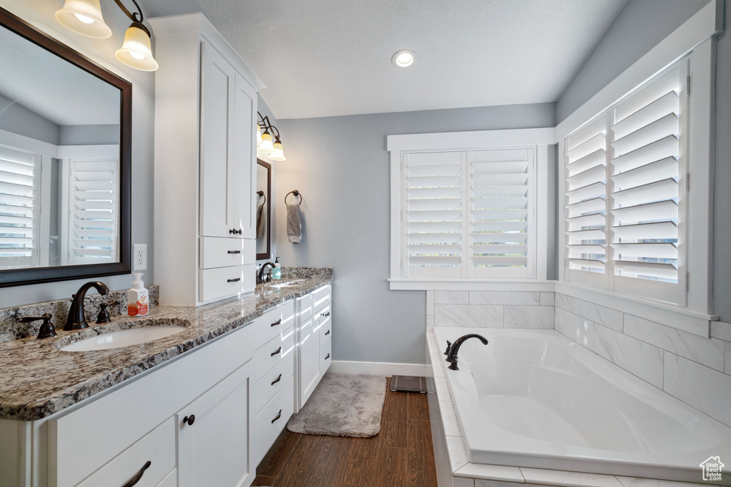 Bathroom featuring plenty of natural light, double sink, large vanity, and tiled bath