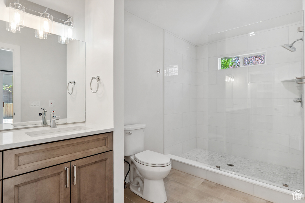 Bathroom featuring vanity with extensive cabinet space, tiled shower, toilet, and a wealth of natural light