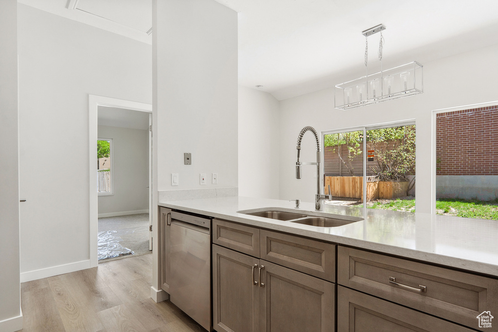 Kitchen with sink, a notable chandelier, stainless steel dishwasher, hanging light fixtures, and light hardwood / wood-style flooring