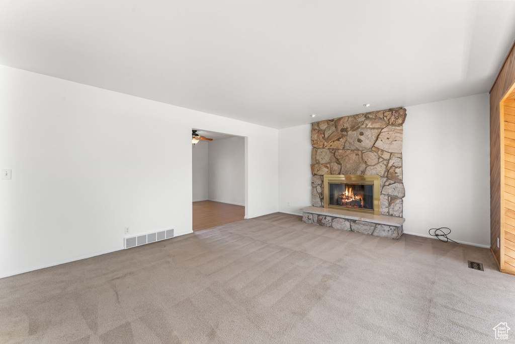 Unfurnished living room featuring light colored carpet, ceiling fan, and a fireplace