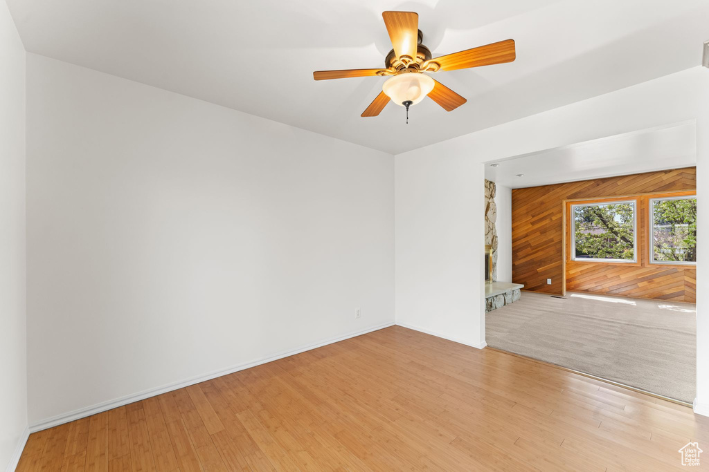 Unfurnished room with light hardwood / wood-style flooring, wood walls, and ceiling fan