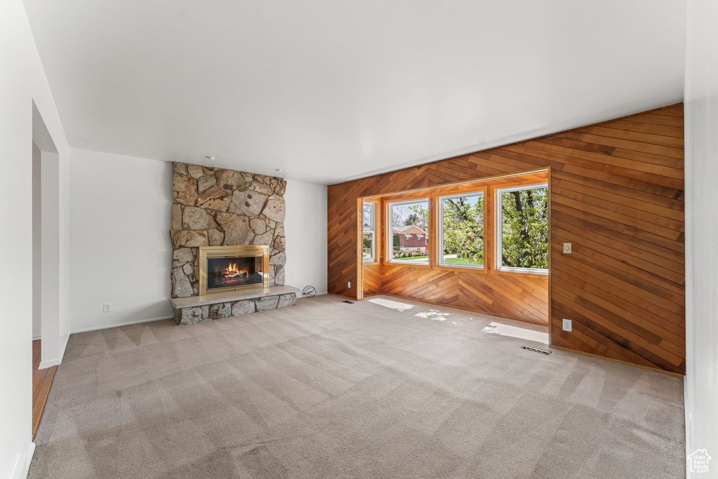 Unfurnished living room featuring wood walls, light colored carpet, and a fireplace