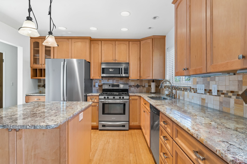 Kitchen featuring light stone countertops, stainless steel appliances, light hardwood / wood-style floors, tasteful backsplash, and sink