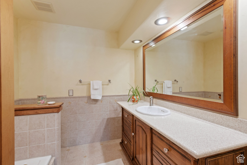 Bathroom featuring a washtub, tile flooring, vanity, and tile walls