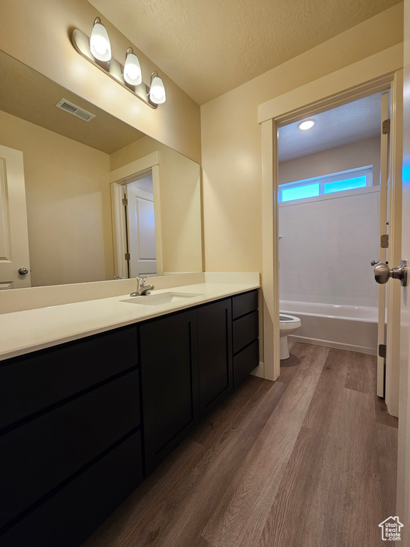 Full bathroom featuring vanity, hardwood / wood-style flooring, shower / bath combination, toilet, and a textured ceiling