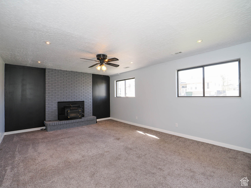 Unfurnished living room featuring a textured ceiling, carpet floors, ceiling fan, and a brick fireplace
