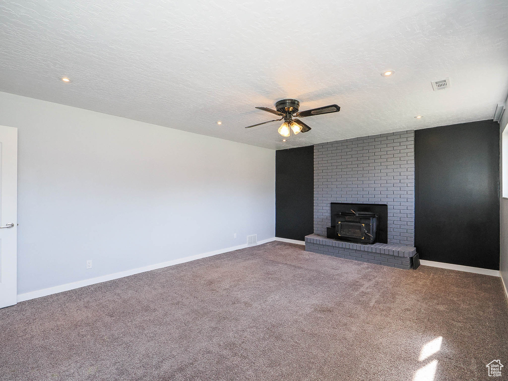 Unfurnished living room featuring ceiling fan, carpet, a fireplace, and a textured ceiling