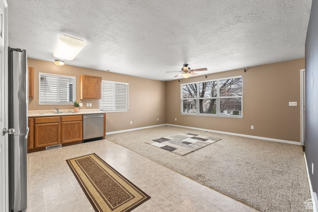 Interior space featuring ceiling fan, stainless steel appliances, a textured ceiling, light carpet, and sink