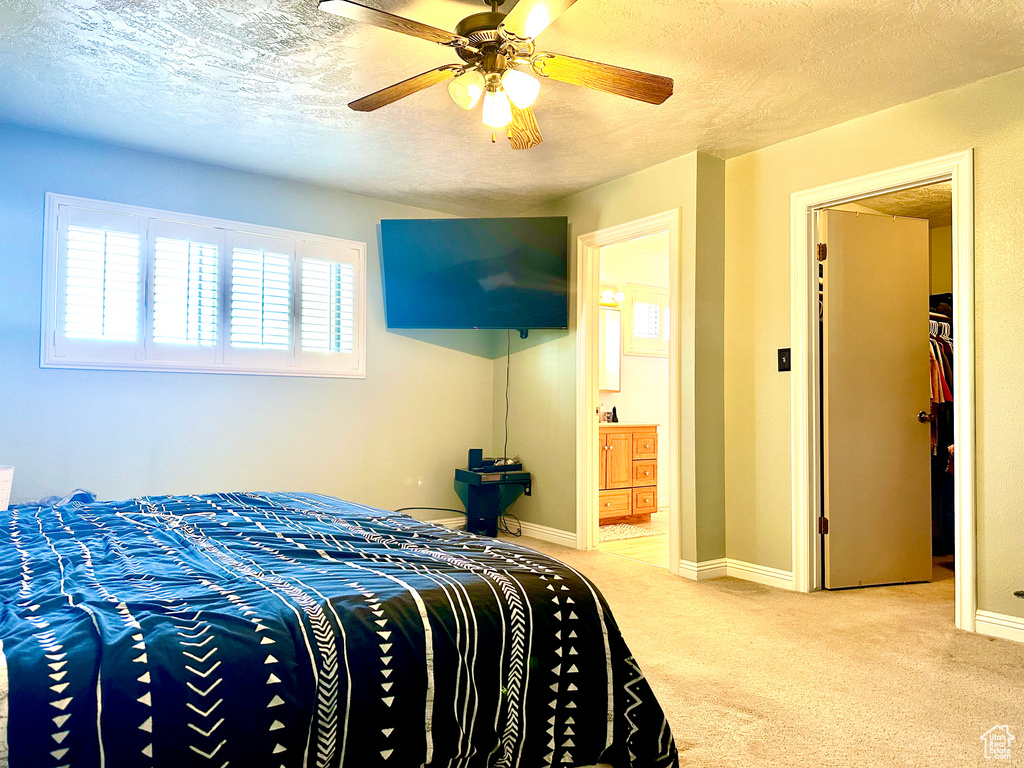 Bedroom featuring light colored carpet, ceiling fan, ensuite bathroom, and a textured ceiling