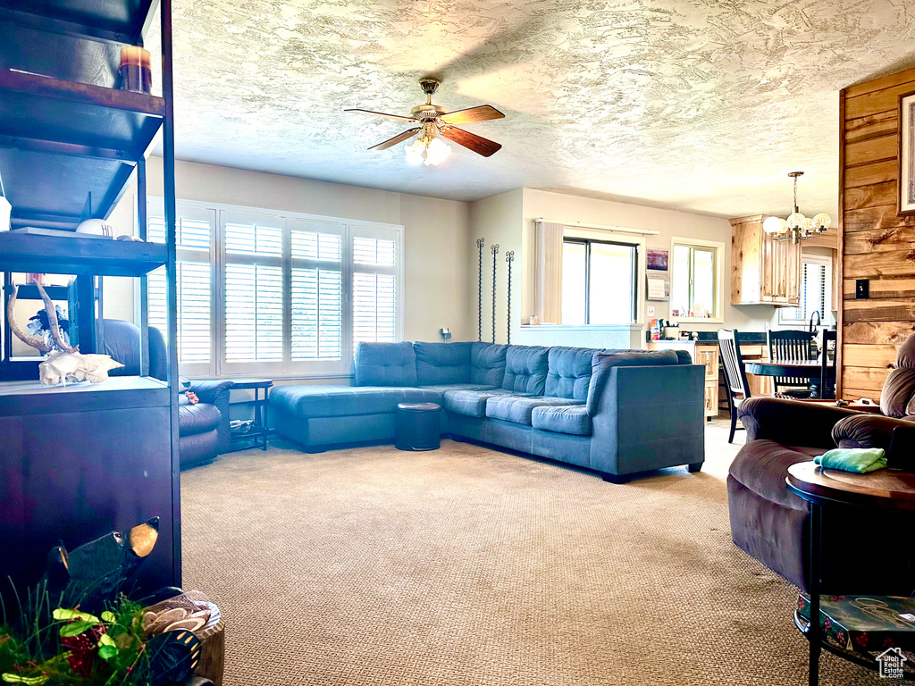 Carpeted living room featuring ceiling fan with notable chandelier and a textured ceiling