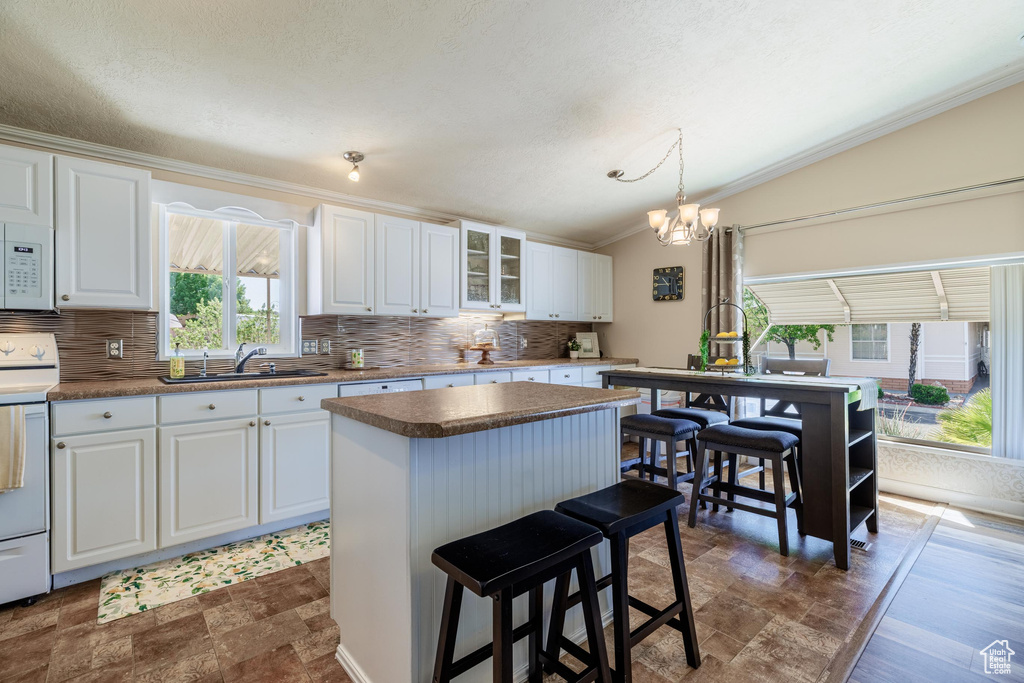 Kitchen featuring a kitchen island, white cabinets, backsplash, decorative light fixtures, and lofted ceiling