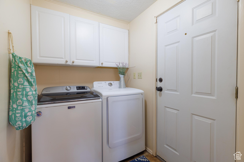 Washroom featuring washer and clothes dryer, cabinets, and a textured ceiling