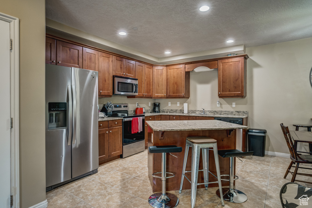 Kitchen with appliances with stainless steel finishes, a center island, light tile floors, and a breakfast bar