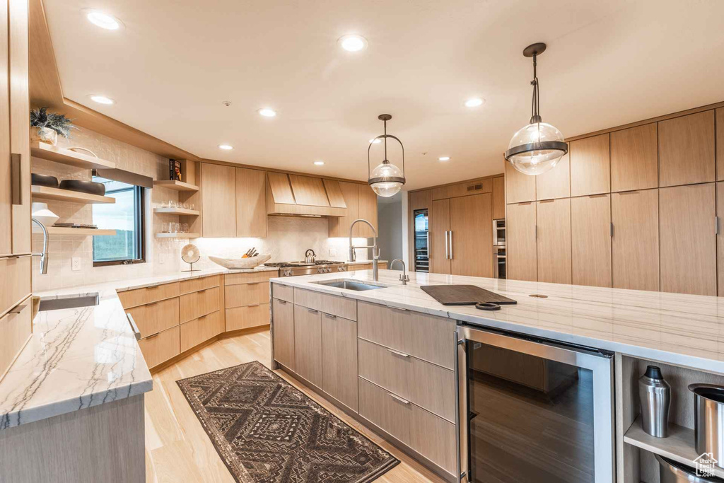 Kitchen with light stone counters, custom exhaust hood, wine cooler, decorative light fixtures, and light hardwood / wood-style flooring