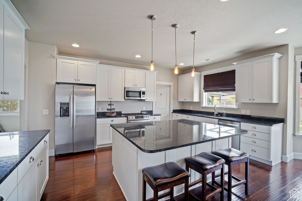 Kitchen featuring appliances with stainless steel finishes, a center island, white cabinetry, dark hardwood / wood-style flooring, and pendant lighting
