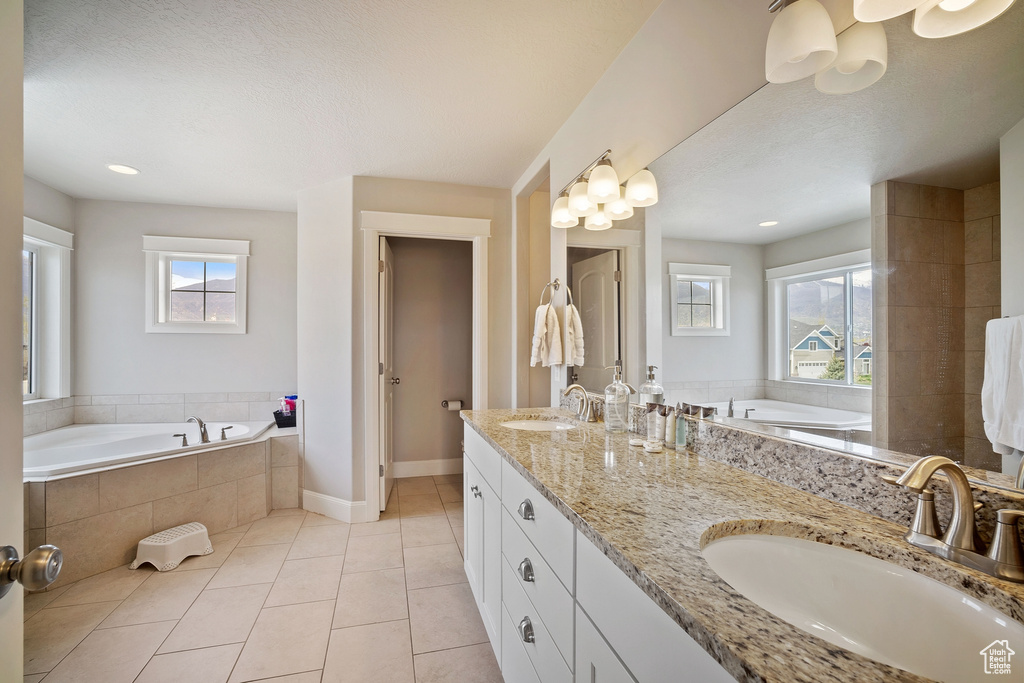 Bathroom with plenty of natural light, a relaxing tiled bath, dual bowl vanity, and tile flooring
