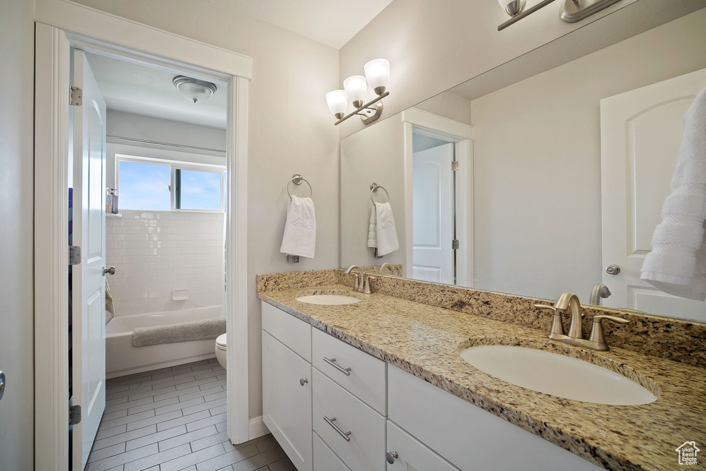 Full bathroom with double sink vanity, tiled shower / bath, toilet, and tile floors