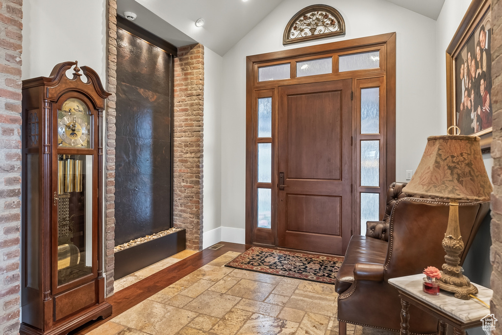 Entryway with lofted ceiling, brick wall, and dark tile flooring